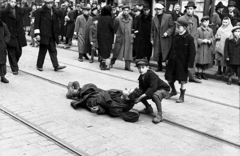 Żydowski chłopiec podnosi głowę zmarłego, który umiera z głodu w getcie warszawskim w okupowanej przez Niemców Polsce, 1942