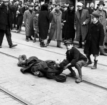 Żydowski chłopiec podnosi głowę zmarłego, który umiera z głodu w getcie warszawskim w okupowanej przez Niemców Polsce, 1942