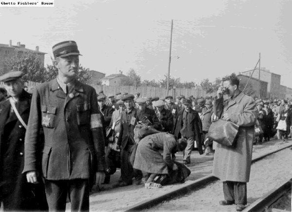 Na zdjęciu członek Jüdischer Ordnungsdienst o nazwisku Śmietana eskortuje swoich braci na śmierć do Auschwitz